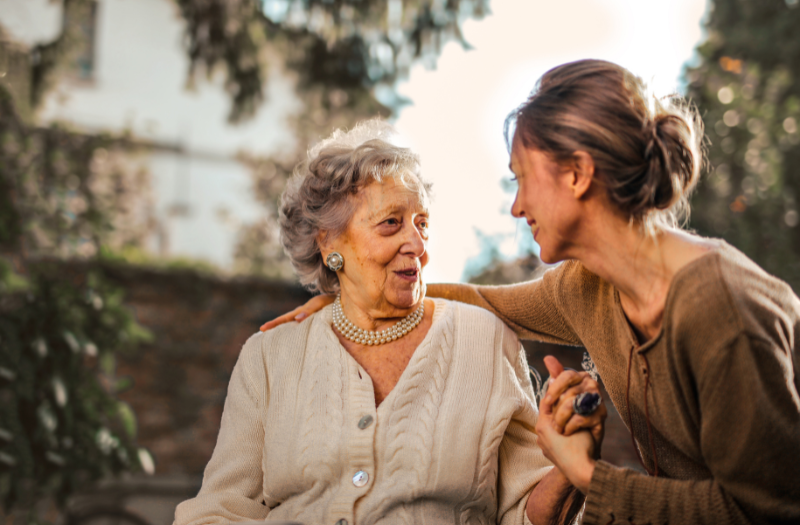 Candid image of an old woman and her daughter smiling at each other and holding hands