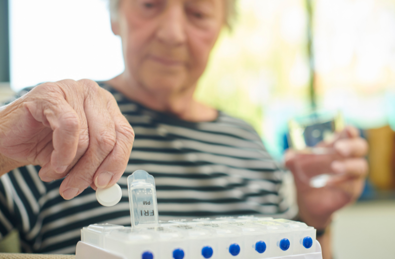 Elderly woman putting her medications into a pill organizer for each day of the week
